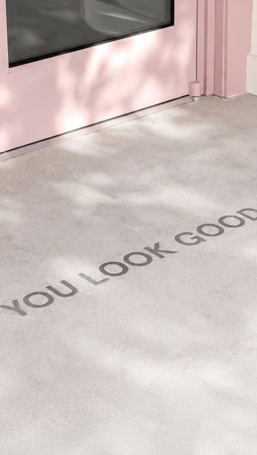 Partial view of a pink door with the motivational text 'YOU LOOK GOOD' on the floor inside a studio or indoor space